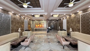 Eine großzügige Lobby mit Marmorboden, zwei Sofas, einem Empfangstresen und Deckenventilatoren.