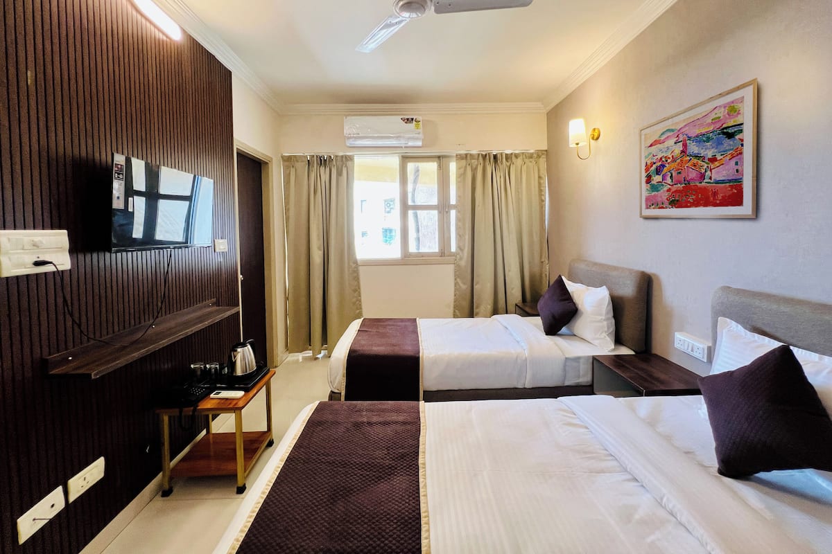 A hotel room with two beds, a TV, a ceiling fan, and a painting on the wall.