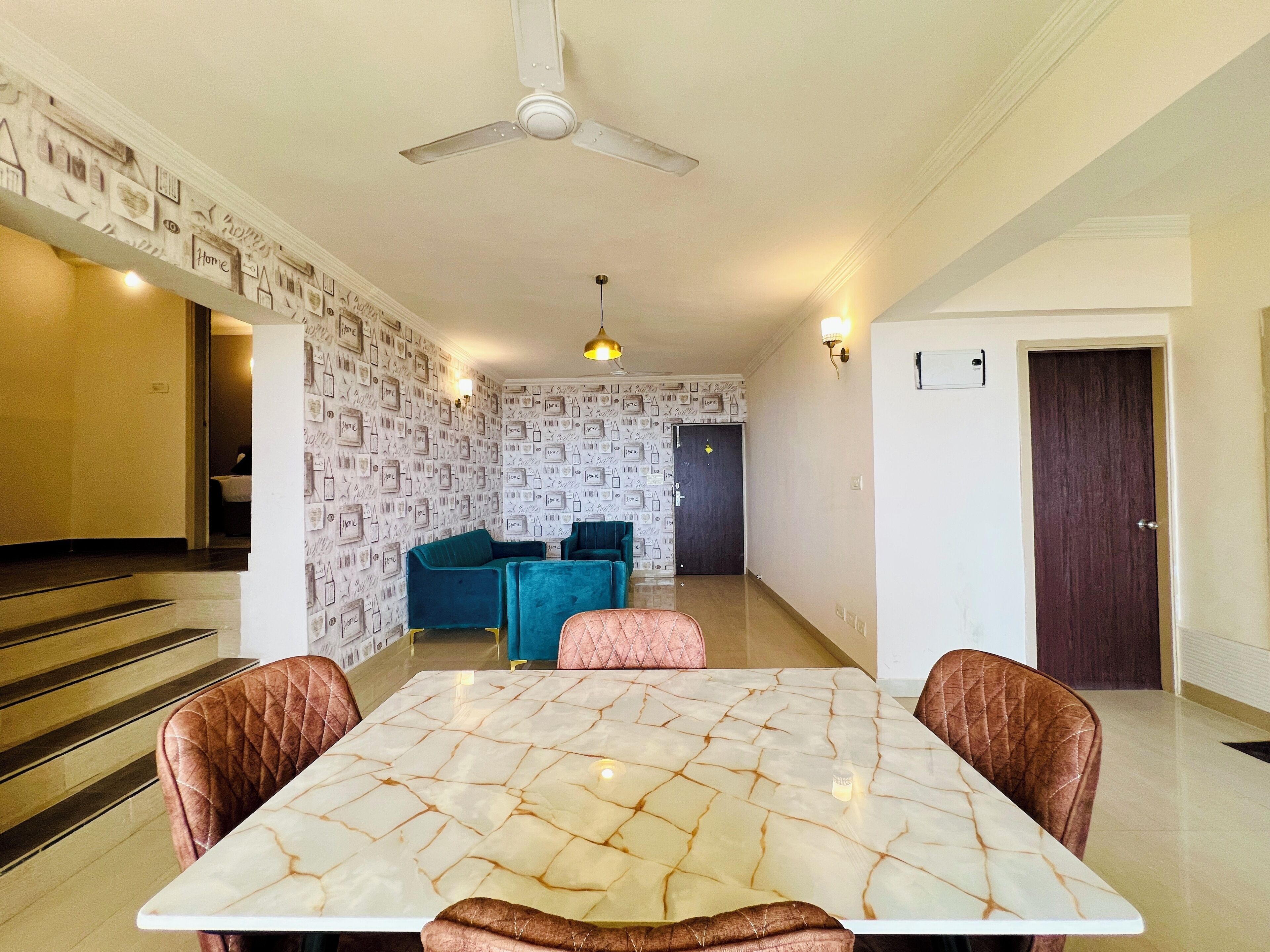 A dining area with a marble table, cushioned chairs, a ceiling fan, and a wall with a pattern of framed pictures.
