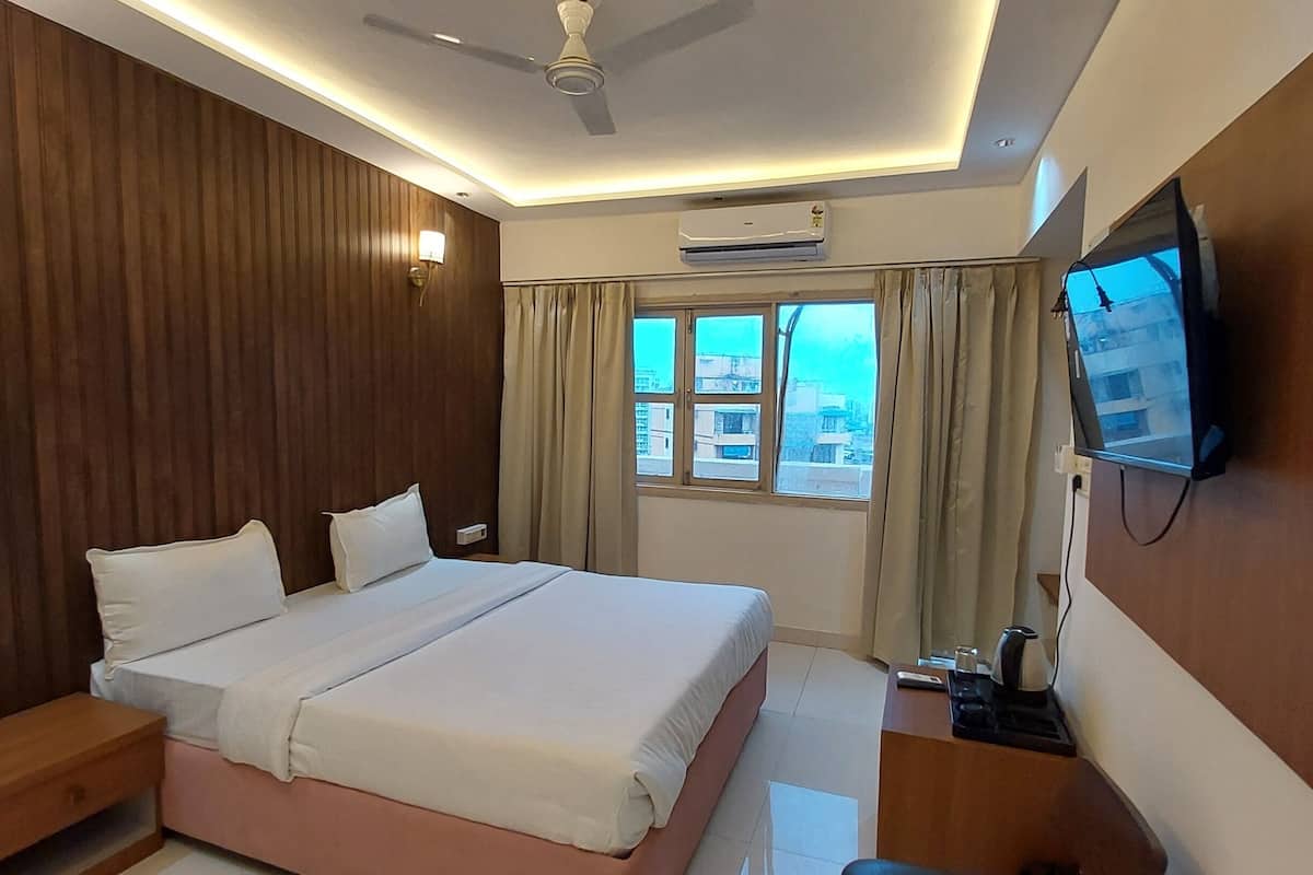 A hotel room with a bed, bedside table, chair, TV, air conditioning unit, and a window with curtains.