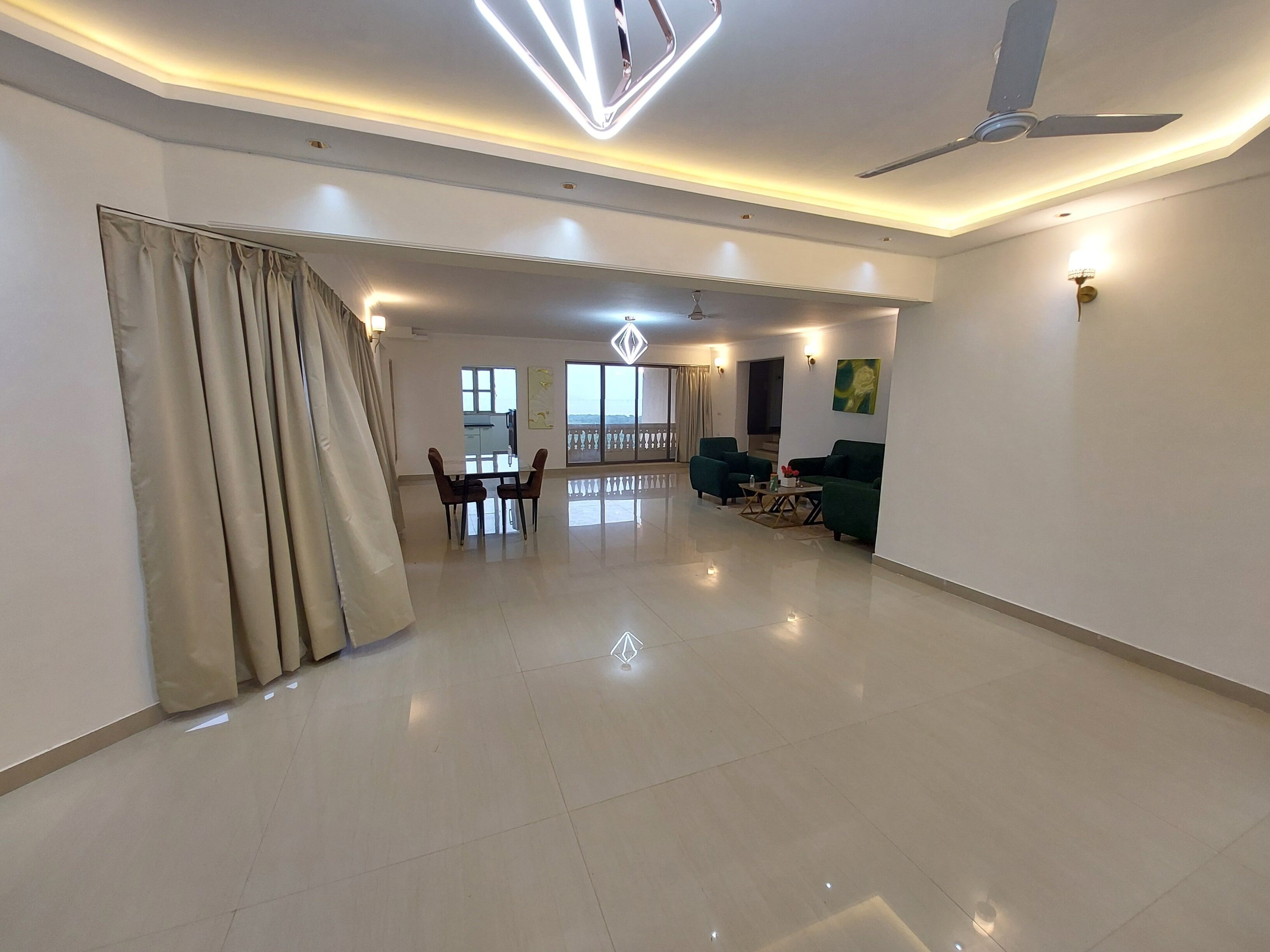 A spacious living area with a dining table, two sofas, a ceiling fan, and a balcony view.