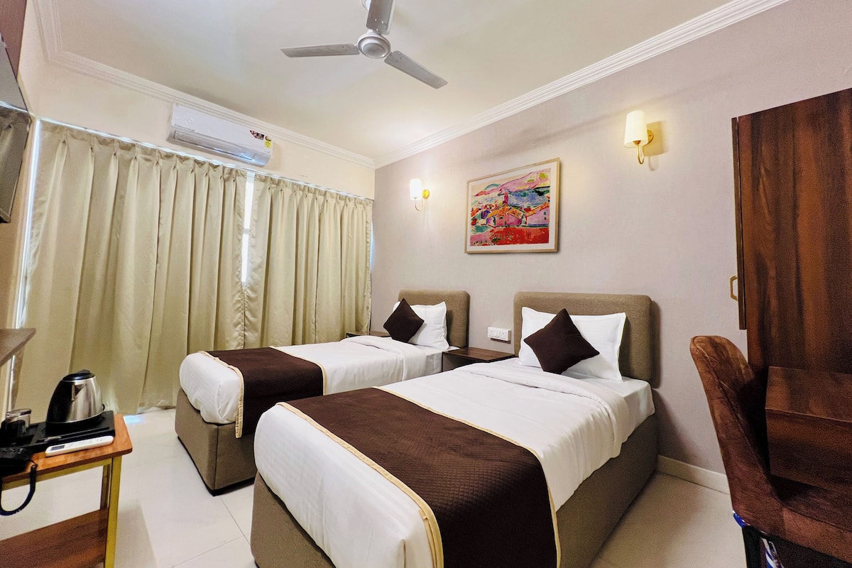 A hotel room with two beds, a ceiling fan, an air conditioning unit, a painting on the wall, and a desk with a coffee maker.