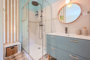 Ein modernes Badezimmer mit einer gläsernen Duschkabine, einem runden Spiegel und hellblauen Schränken.