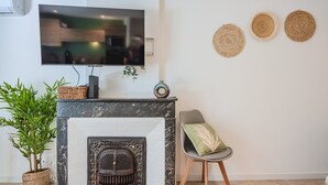 Un salon moderne doté d’une cheminée, d’un téléviseur à écran plat fixé au-dessus, et d’un coin salon comprenant un fauteuil et une petite table.