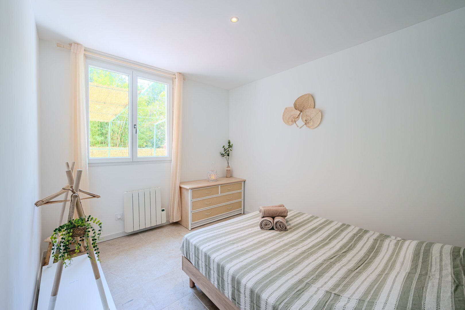 A bedroom with a bed, dresser, radiator, window, and a plant.