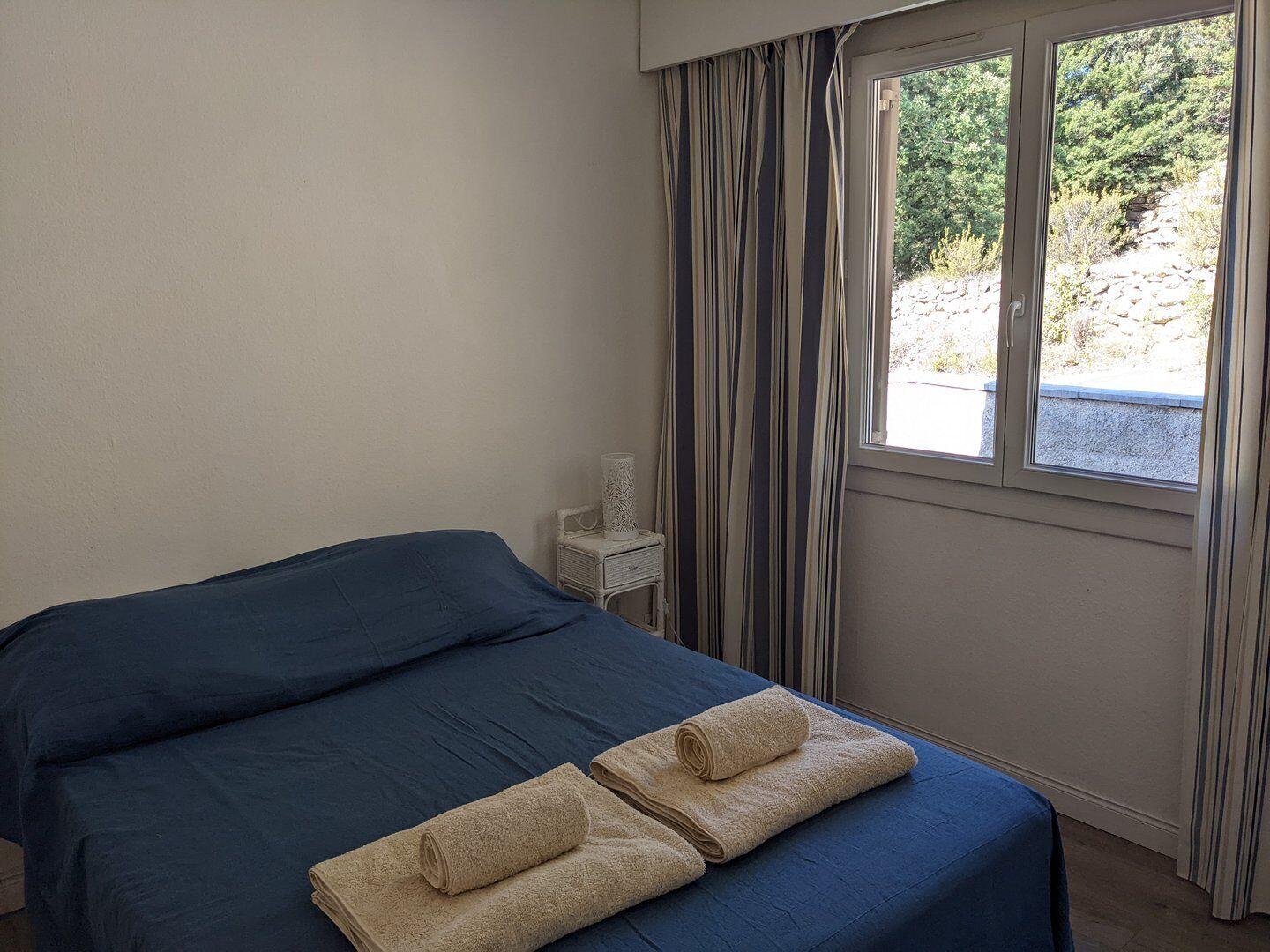 Une chambre à coucher avec un lit, une fenêtre avec des rideaux et une table de chevet avec une lampe.
