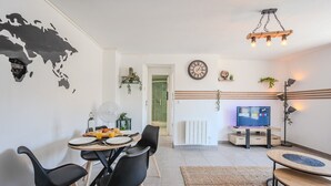 A modern living room with a dining area, featuring a world map wall art, a wooden dining table, black chairs, a TV, and a floor lamp. - The Port Marchand Escapade - Air-conditioned flat (Toulon)