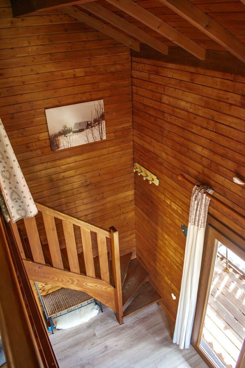 Un escalier en bois menant à un niveau inférieur, une fenêtre avec des rideaux et un tableau accroché au mur.