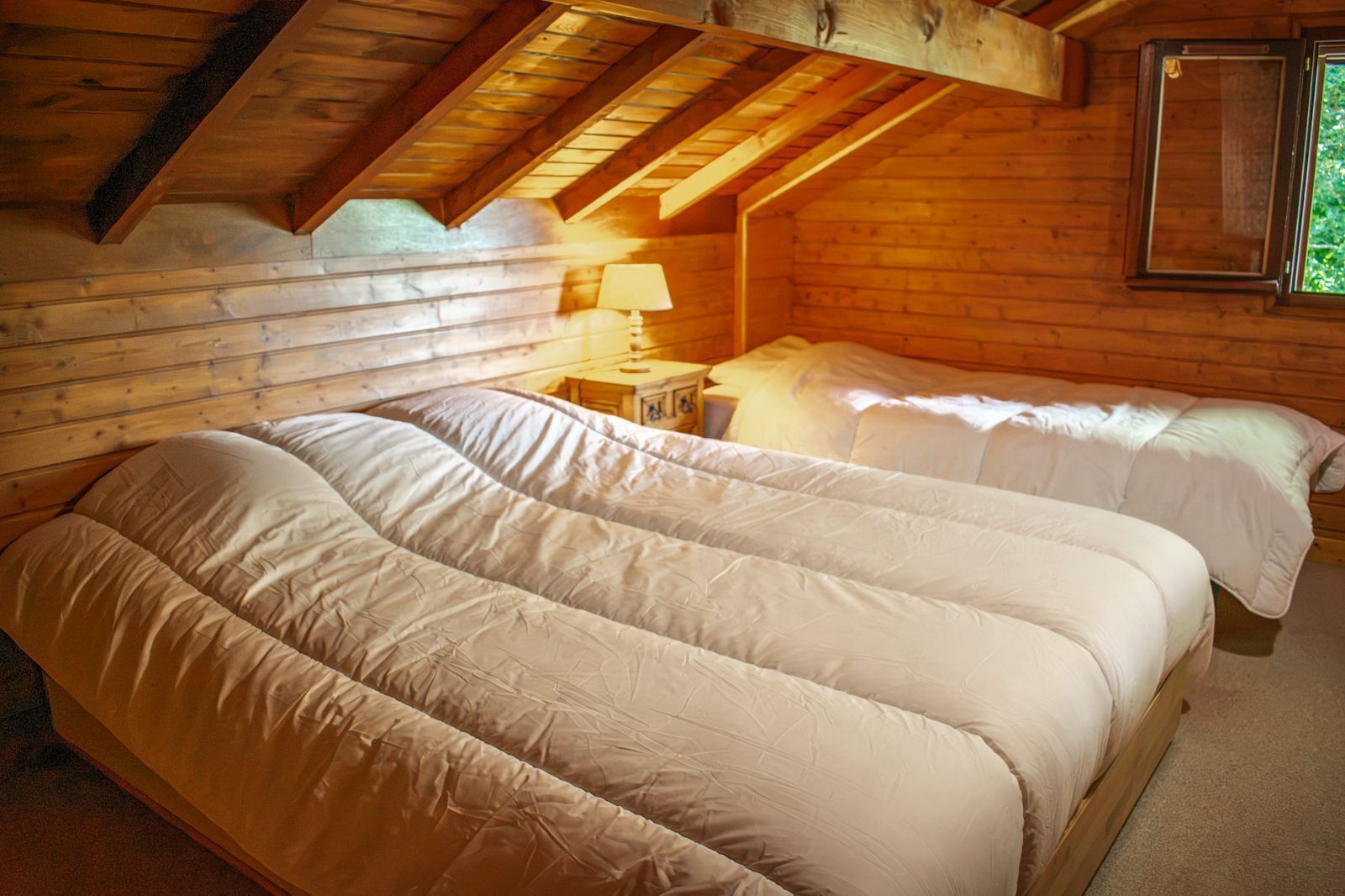 Une pièce confortable avec un plafond en bois, un grand lit avec deux oreillers, une table de chevet avec une lampe et une fenêtre.