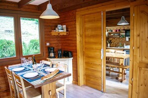 A wooden interior with a dining table set for two, a coffee maker, and a kitchen area visible through an open door. - Entire chalet, panoramic views, stream and sauna. (Bussang)