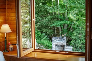 A wooden cabin interior with a large window overlooking a dense forest and a stone fireplace. - Entire chalet, panoramic views, stream and sauna. (Bussang)
