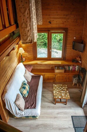 A cozy cabin interior with a bed, a small table, and a window overlooking greenery. - Entire chalet, panoramic views, stream and sauna. (Bussang)