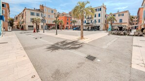 A sunny urban square with palm trees, cafes, and buildings with signage like "URGENCE PHONE". - Charming Apartment - Panoramic Harbor View (La Seyne-sur-Mer)