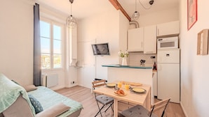 A compact living space with a bed, a dining table with breakfast, a TV, and a kitchenette. - Charming Apartment - Panoramic Harbor View (La Seyne-sur-Mer)