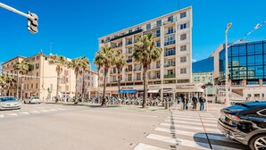 Una intersección de calles con paso de peatones, palmeras y edificios con tiendas y restaurantes.