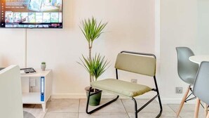 Ein modernes Wohnzimmer mit Flachbildfernseher, Topfpflanze, Sessel und kleinem Tisch.