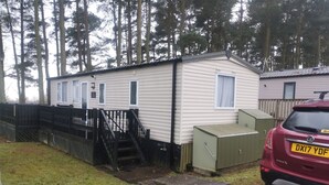 Ett hus på hjul med en inhägnad trädgård, en trappa som leder upp till entrén och en parkerad bil.