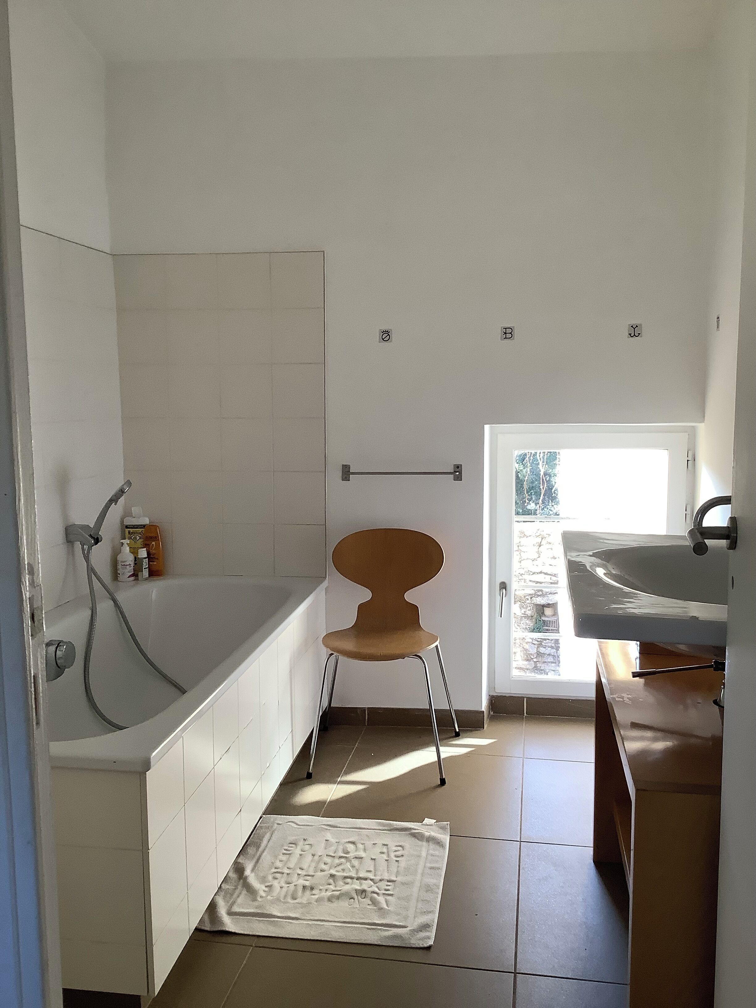 A bathroom with a bathtub, a shower, a towel rack, and a chair.