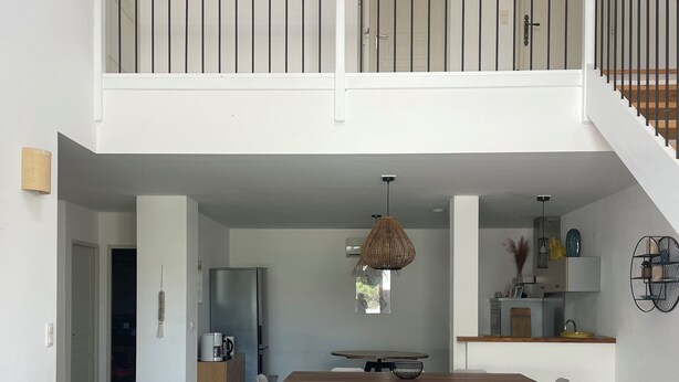 Un vaste espace de vie doté d’un haut plafond, une table à manger avec des chaises, un canapé, une table basse et un escalier menant à un niveau supérieur.
