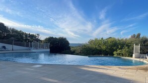 Une piscine avec vue sur l’océan, entourée de verdure et sous un ciel dégagé.