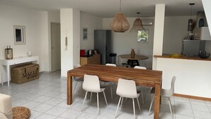 Une cuisine moderne avec des meubles blancs, une table à manger en bois et un luminaire suspendu.