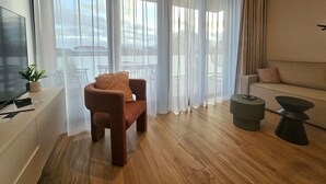 A modern living room with a wooden floor, a brown armchair, a sofa, a TV, and a small side table.