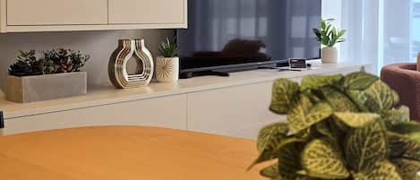 A modern living room with a flat-screen TV, a coffee table, and decorative plants.