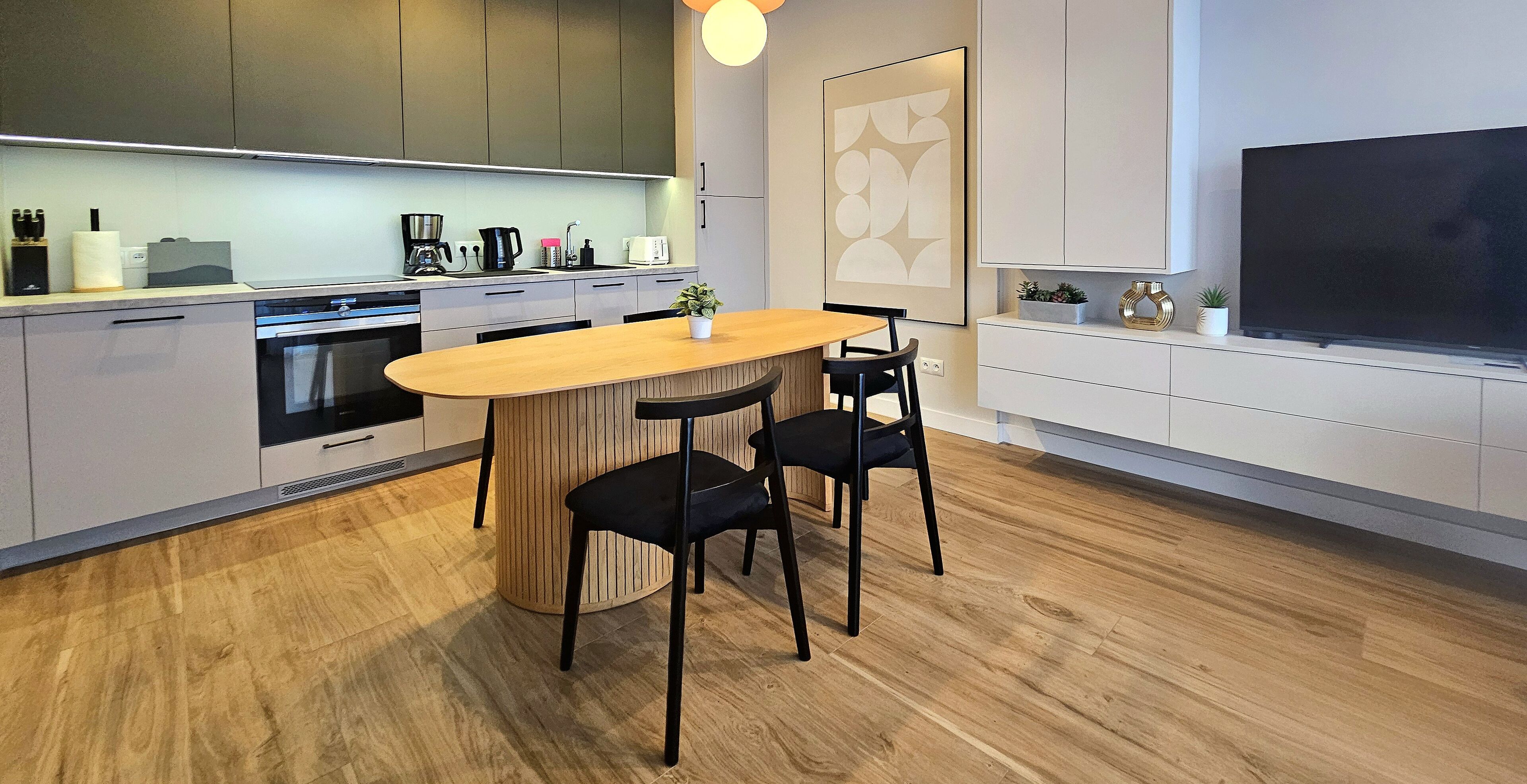 Una cucina moderna con isola centrale, pavimento in legno e un grande televisore piatto montato a parete.