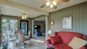 A living room with a red sofa, a ceiling fan, and a dining area with white chairs and a table. - Cozy Beach Retreat with Tennis! Short walk to the beach! (Hilton Head Island)