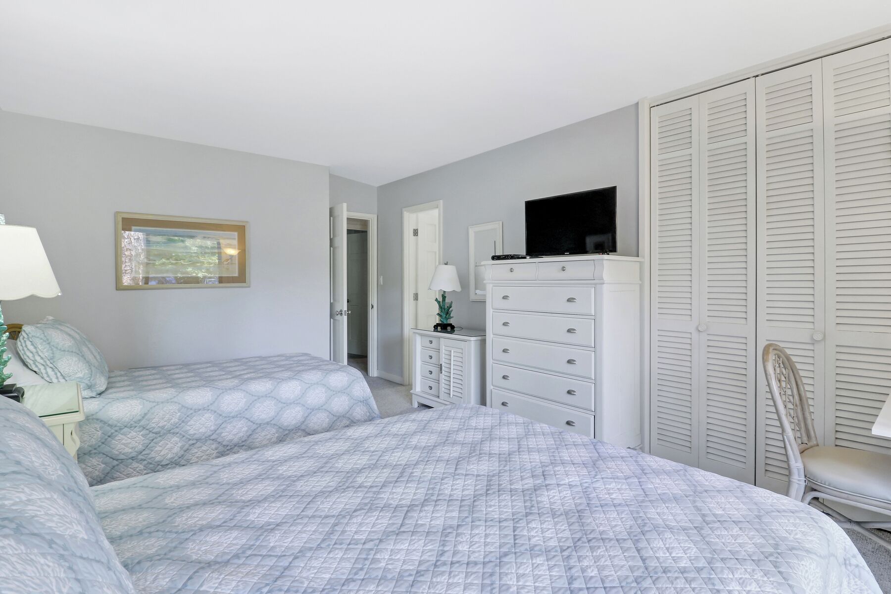 A bedroom with two beds, a dresser, a television, and a chair.