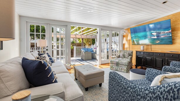 A spacious living room with a large TV, comfortable seating, and a view of the outdoors. - CASA DEL SUR ~ Renovated 2 BR/2Ba Home with Heated Dip Pool! (Key West)