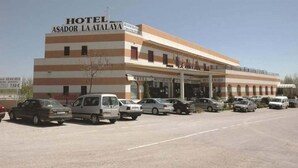 A hotel with a sign reading "HOTEL ASADOR LA ATALAYA" and "RESTAURANTE CONVENIENTES". There are multiple cars parked in front.