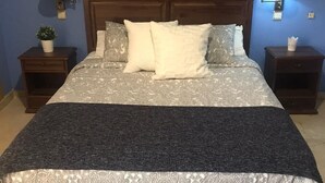 A neatly made bed with patterned bedding and a dark throw blanket. There are two bedside tables, each with a lamp and a small plant.