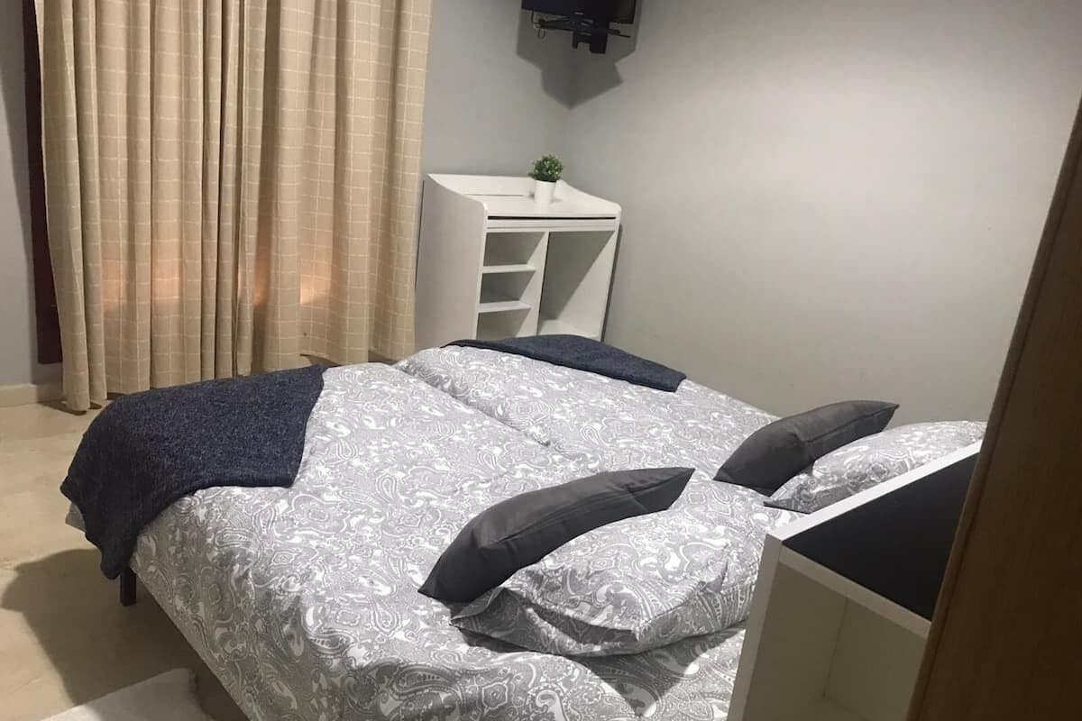 A bedroom with a bed, a desk, and a small plant.