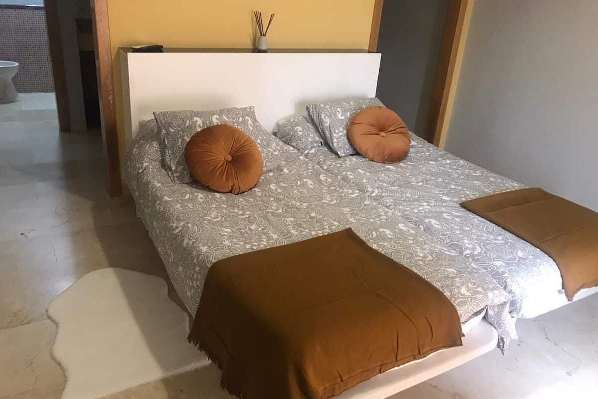 A bed with patterned bedding and two brown pillows, a white headboard, and a brown throw blanket.