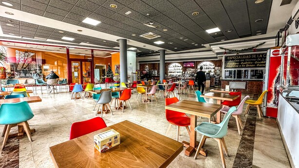 A spacious indoor dining area with multiple tables and colorful chairs, a bar area with bottles, and a Christmas tree.