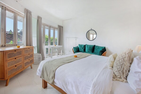 A bedroom with a bed, a wooden dresser, a round mirror, and a view of the outside.