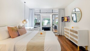 A modern hotel room with a large bed, a white dresser, a round mirror, and a TV on the wall. - Villa Roma (Seminyak)