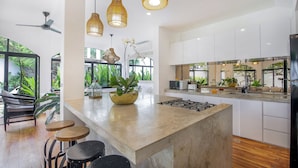 A modern kitchen with a central island, bar stools, hanging wicker lights, and a ceiling fan. - Villa Roma (Seminyak)