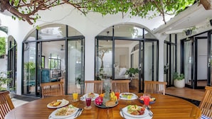 A dining area with a wooden table, chairs, and a variety of dishes and drinks. - Villa Roma (Seminyak)