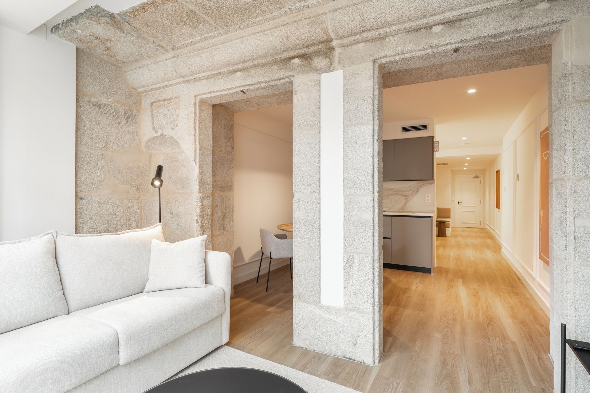 A modern living room with a white sofa, a stone accent wall, and a view into the kitchen area.