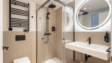 Un baño moderno con ducha envuelta en vidrio, inodoro blanco, lavamanos con espejo y barra para toallas.