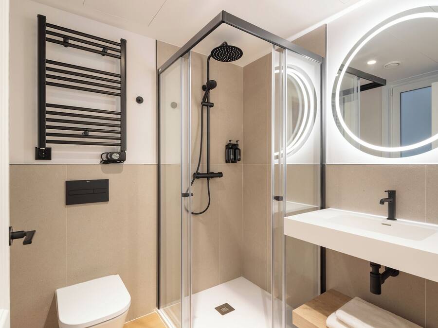 Un baño moderno con ducha envuelta en vidrio, inodoro blanco, lavamanos con espejo y barra para toallas.