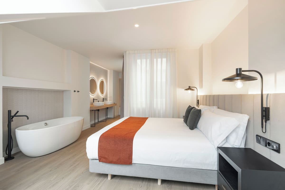 A modern hotel room with a large bed, a separate bathroom with a bathtub, and a vanity with a mirror.