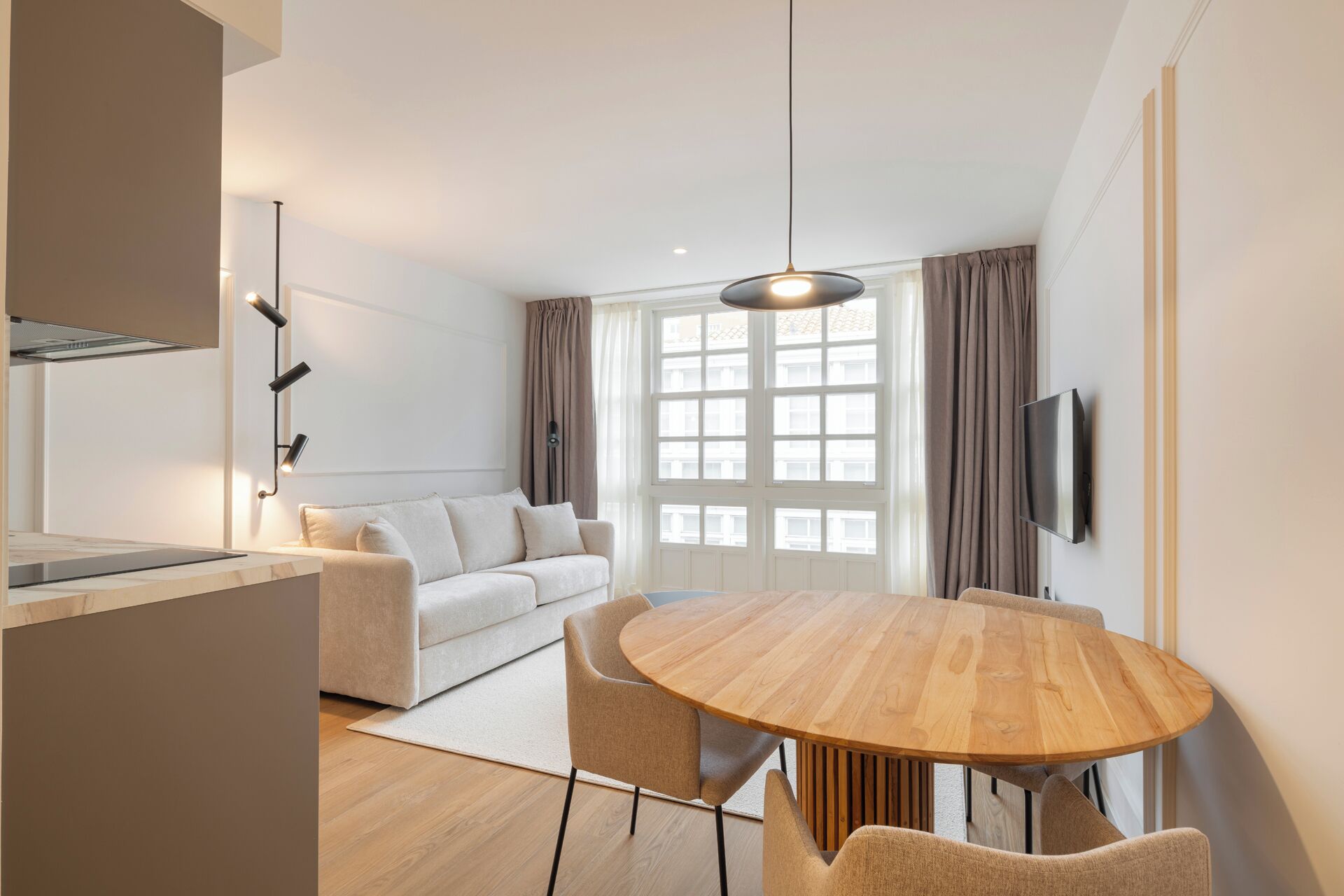 A modern living room with a round wooden dining table, a sofa, and a TV mounted on the wall.