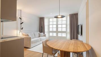 A modern living room with a round wooden dining table, a sofa, and a TV mounted on the wall.