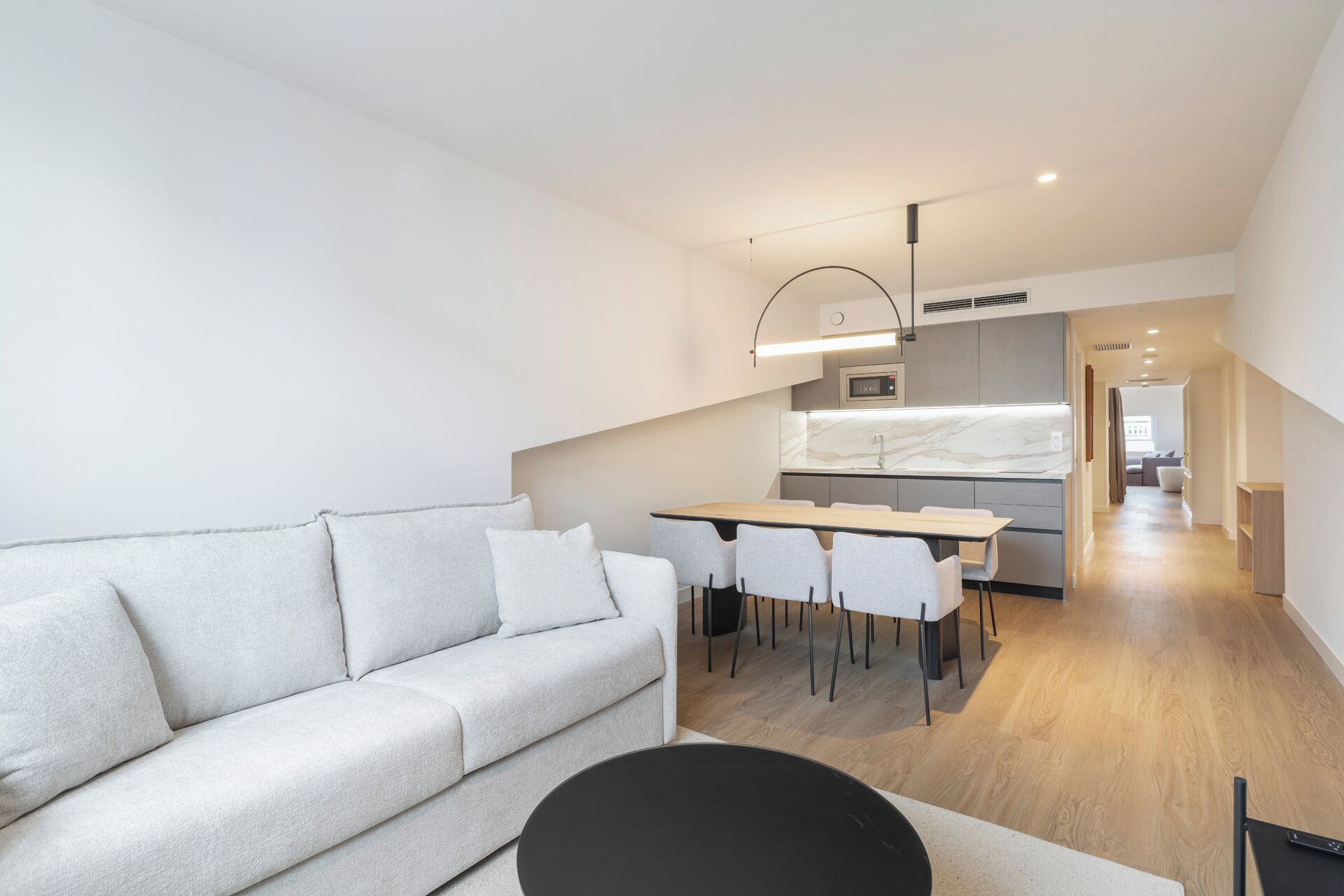 A modern living room with a sofa, a dining table with chairs, and a kitchen area with a marble countertop.