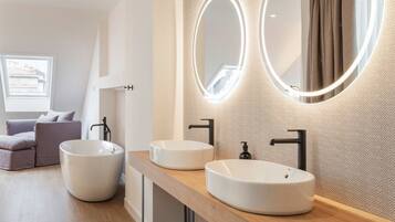 Un baño moderno con dos lavamanos redondos, un espejo grande con iluminación integrada y un mueble de tocador de madera.