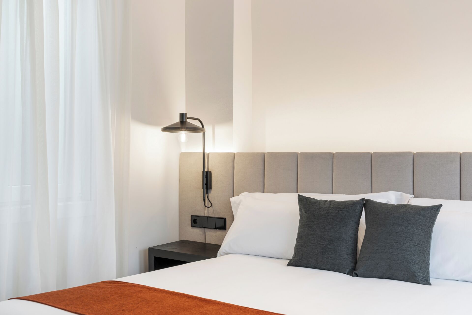 A hotel room with a bed, a nightstand, a lamp, and a window with curtains.