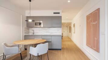 Uma cozinha moderna com bancada de mármore, forno embutido e luminária pendente. Há uma mesa de jantar com duas cadeiras e piso de madeira.